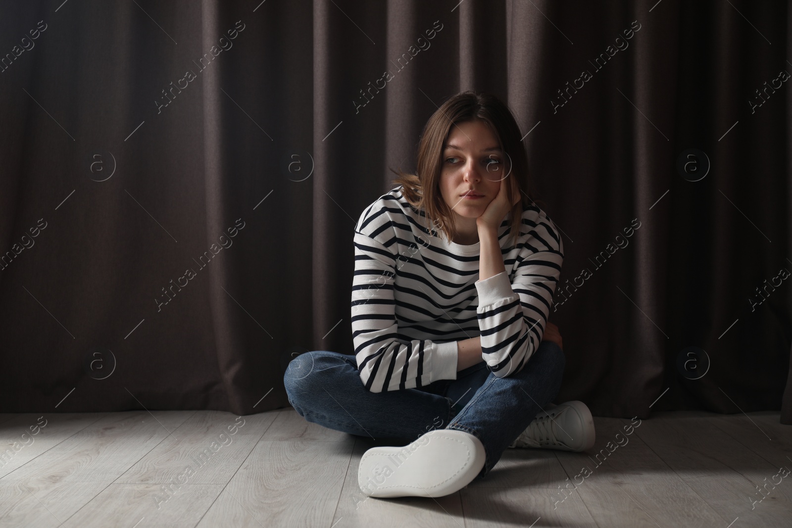 Photo of Sad young woman sitting on floor near curtains