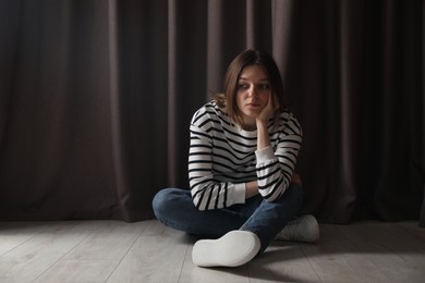 Photo of Sad young woman sitting on floor near curtains