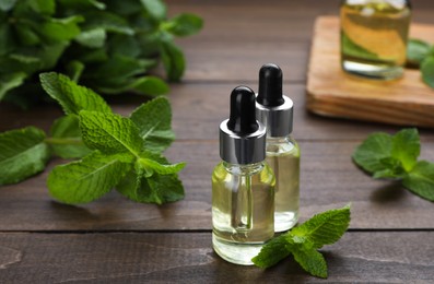 Bottles of essential oil and mint on wooden table, closeup