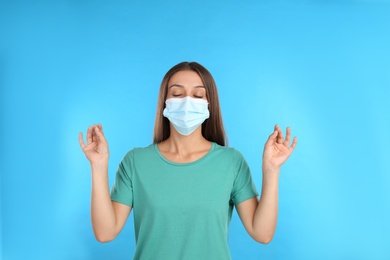 Photo of Woman in protective mask meditating on light blue background. Dealing with stress caused by COVID‑19 pandemic
