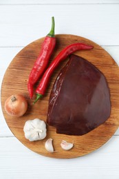 Photo of Piece of raw beef liver with chili peppers, onion and garlic on white wooden table, top view
