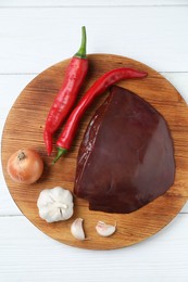 Piece of raw beef liver with chili peppers, onion and garlic on white wooden table, top view