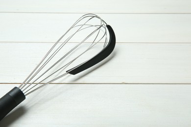 Metal whisk on white wooden table, closeup. Space for text