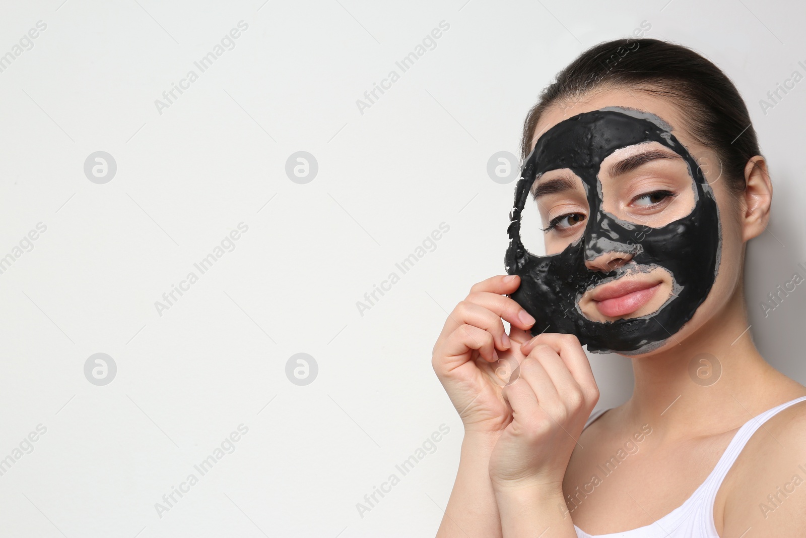 Photo of Beautiful young woman removing black mask from her face on white background. Space for text