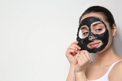 Photo of Beautiful young woman removing black mask from her face on white background. Space for text