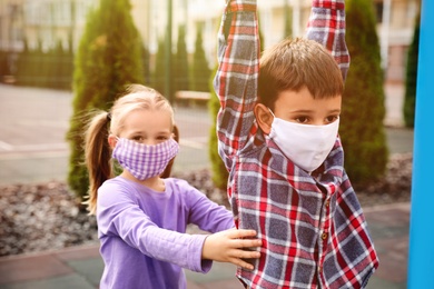 Little children with medical face masks on playground during covid-19 quarantine