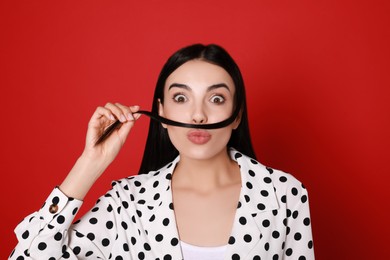 Funny woman making fake mustache with her hair on red background