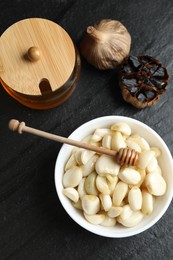 Photo of Garlic with honey in bowl and fermented black garlic on table, flat lay