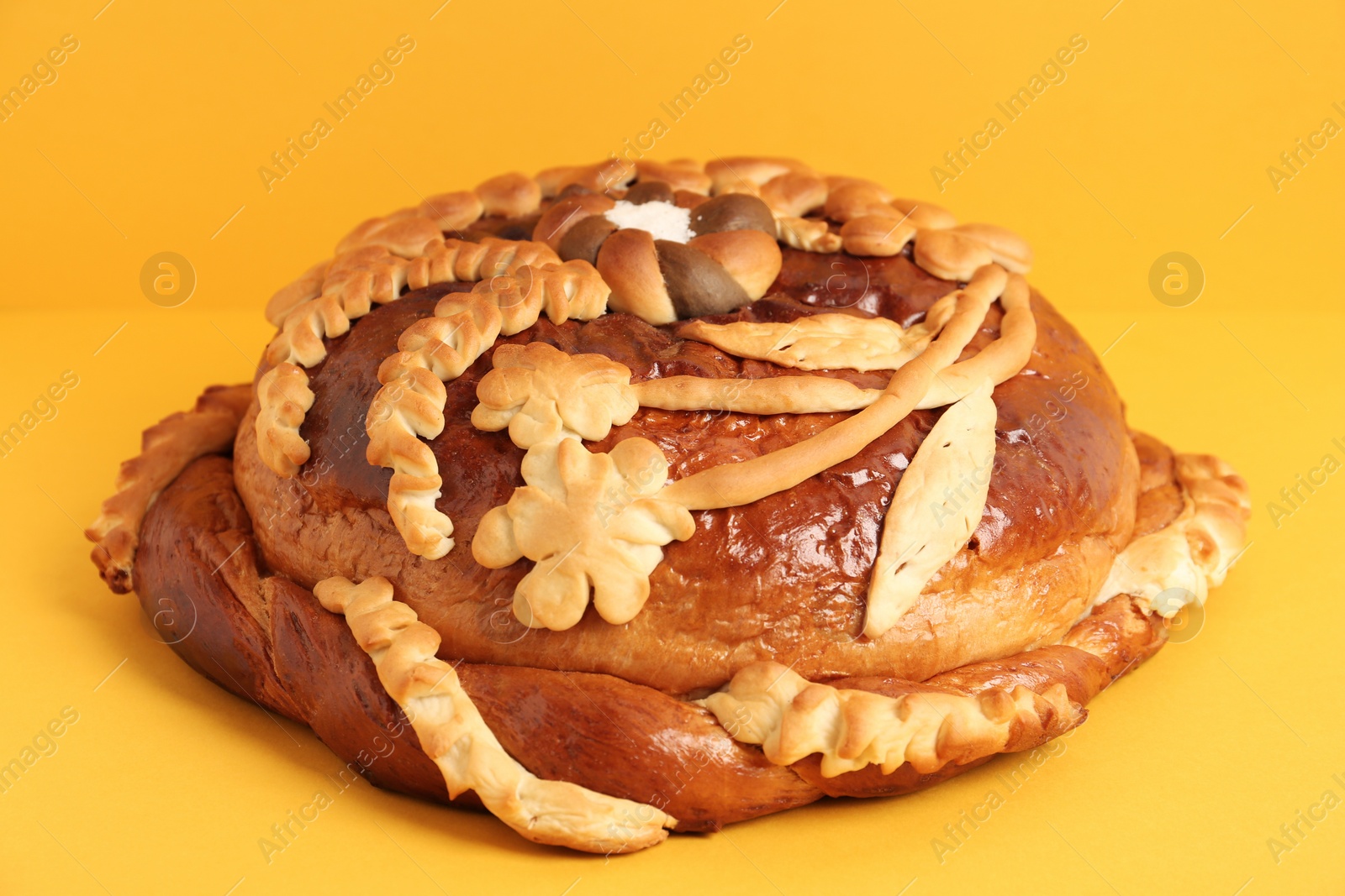 Photo of Fresh korovai on yellow background, closeup. Ukrainian bread and salt welcoming tradition