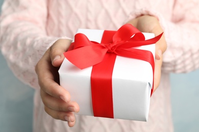 Woman holding beautiful Christmas gift on light blue background, closeup