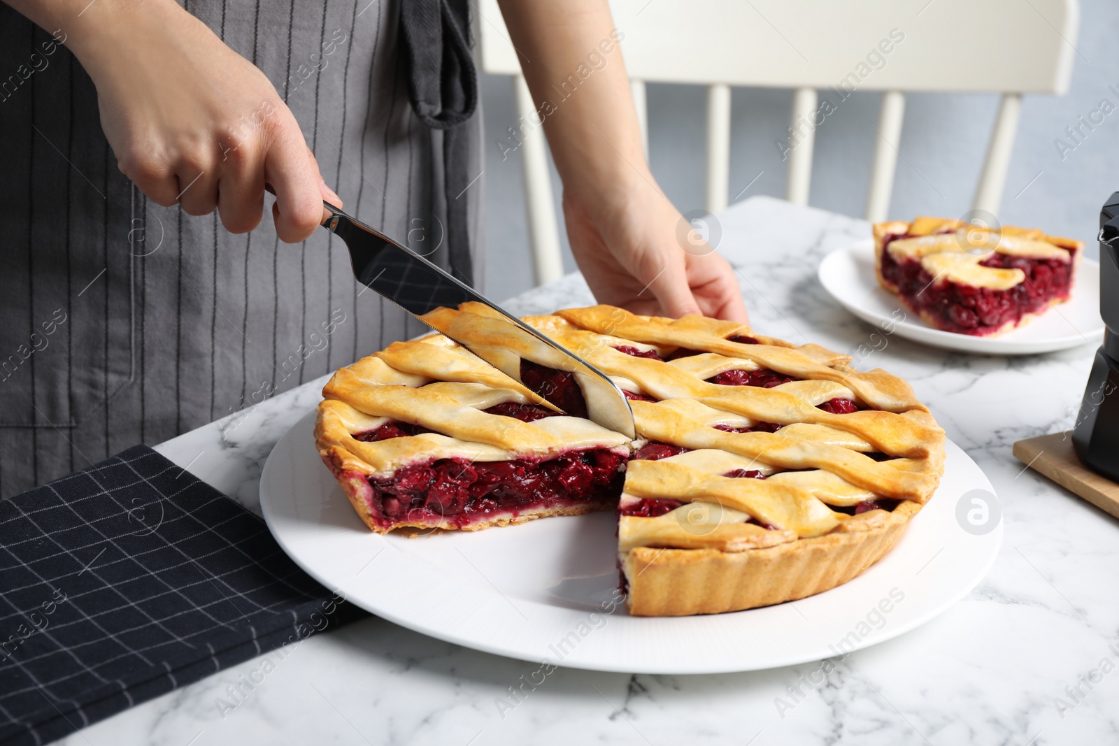 Photo of Woman cutting tasty cherry pie at white marble table, closeup
