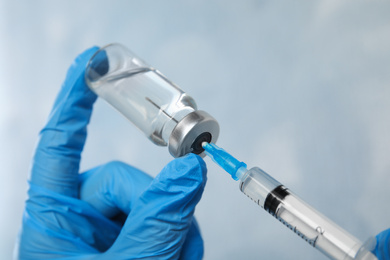 Photo of Doctor filling syringe with medication on light background, closeup. Vaccination and immunization