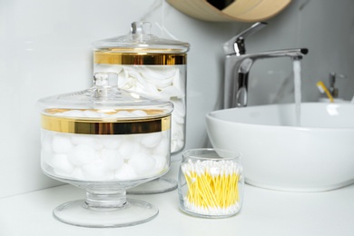 Jars with cotton balls, swabs and pads on white countertop in bathroom