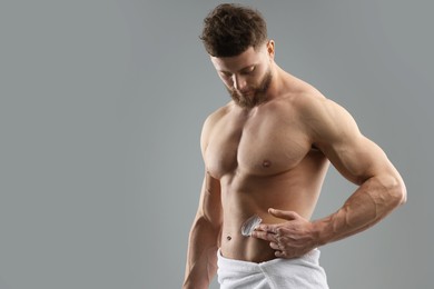 Handsome man applying moisturizing cream onto his body on grey background, space for text