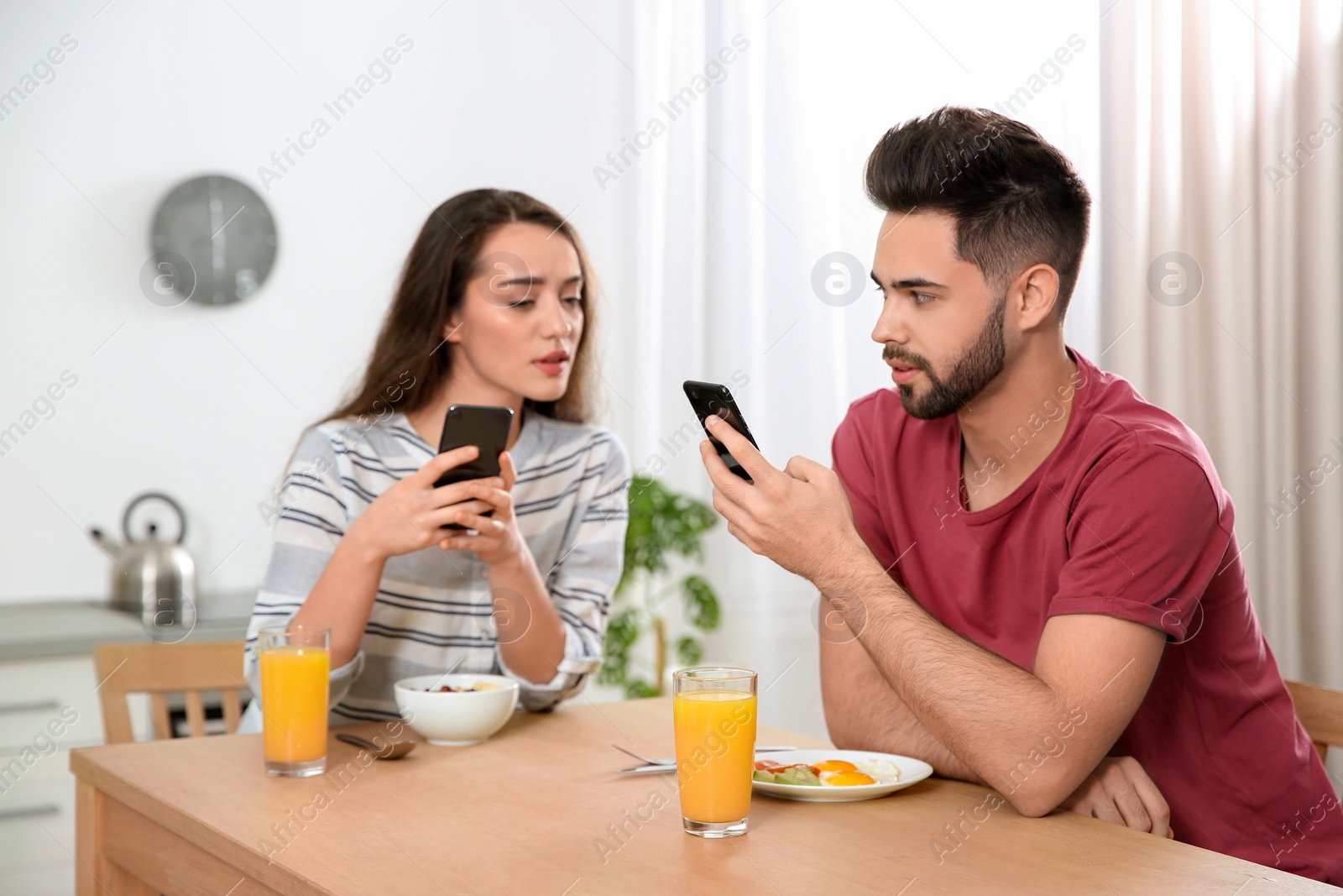 Photo of Distrustful young woman peering into boyfriend's smartphone at home