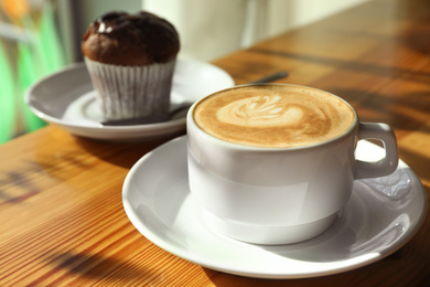 Photo of Cup of fresh aromatic coffee and cupcake at table in cafe