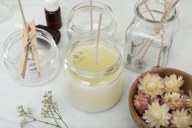 Photo of Glass jar with wax, wick and flowers on white table. Making homemade candle