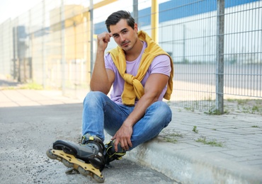 Photo of Handsome young man with inline roller skates sitting on curb outdoors