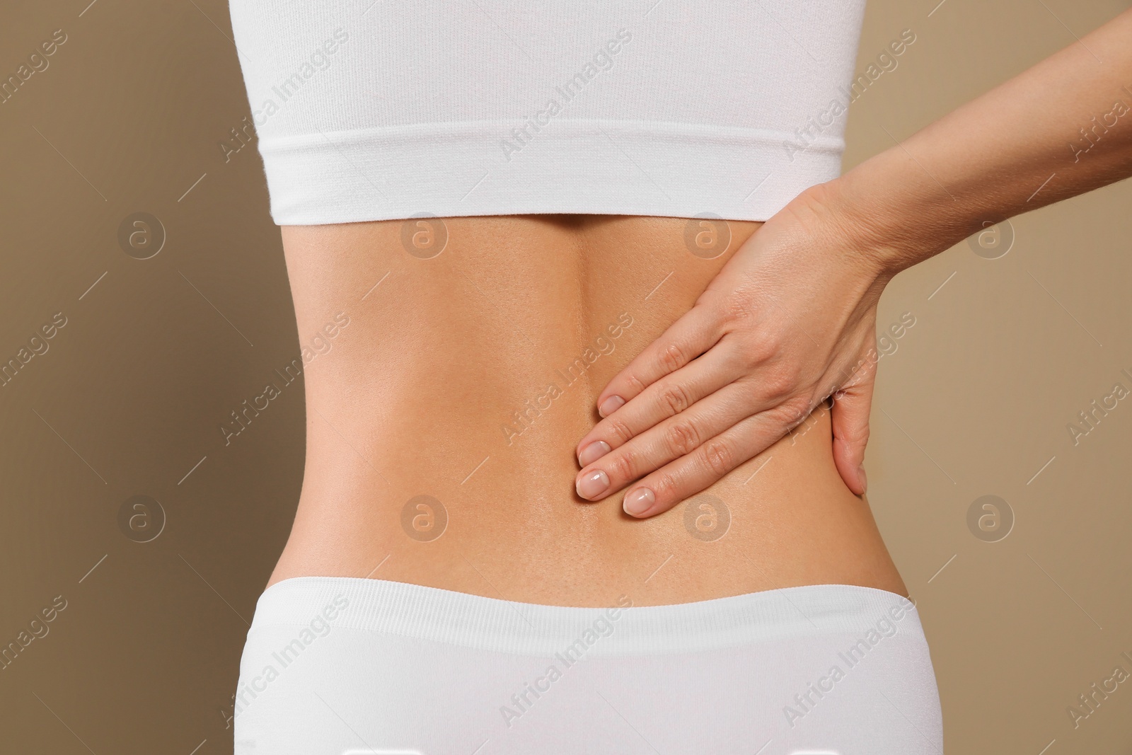 Photo of Woman suffering from pain in back on beige background, closeup