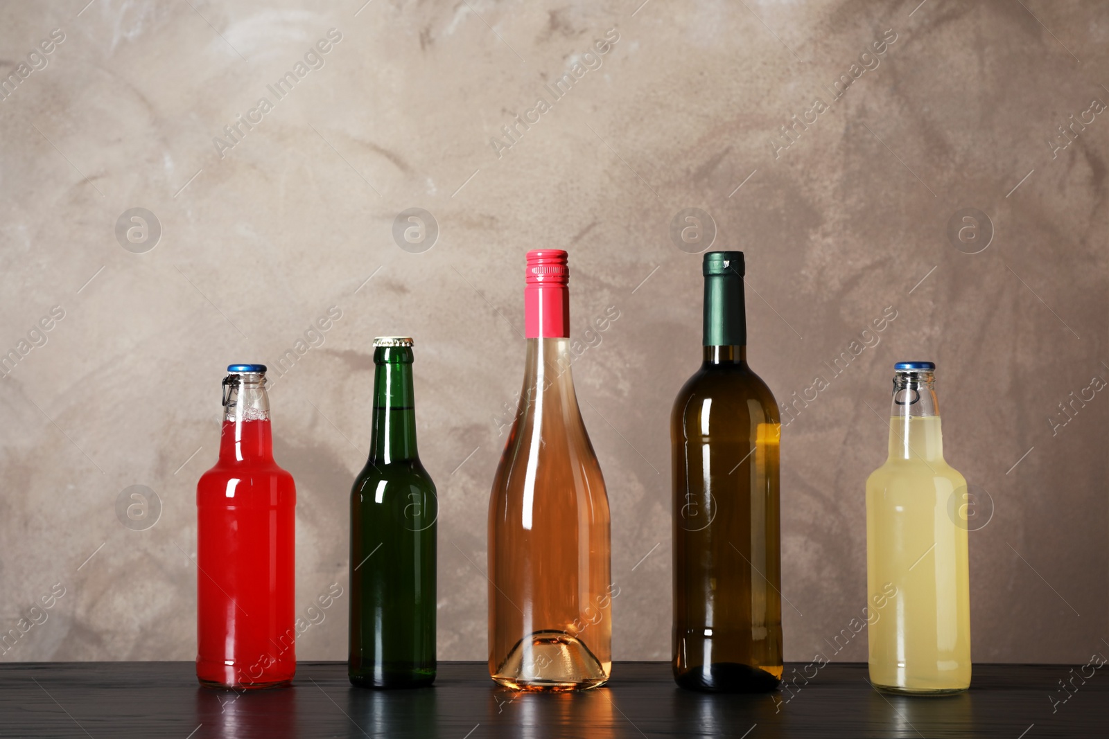 Photo of Bottles with different alcoholic drinks on table against color background