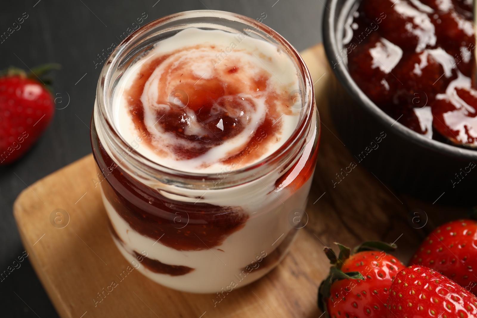 Photo of Tasty yoghurt with jam and strawberries on black table, closeup