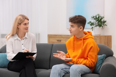 Psychologist working with teenage boy on sofa in office