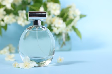 Photo of Aromatic perfume in bottle and beautiful jasmine flowers on light blue background, closeup. Space for text