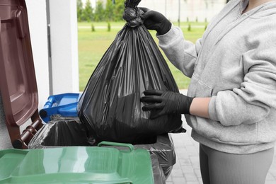 Photo of Woman throwing trash bag full of garbage in bin outdoors, closeup. Recycling concept