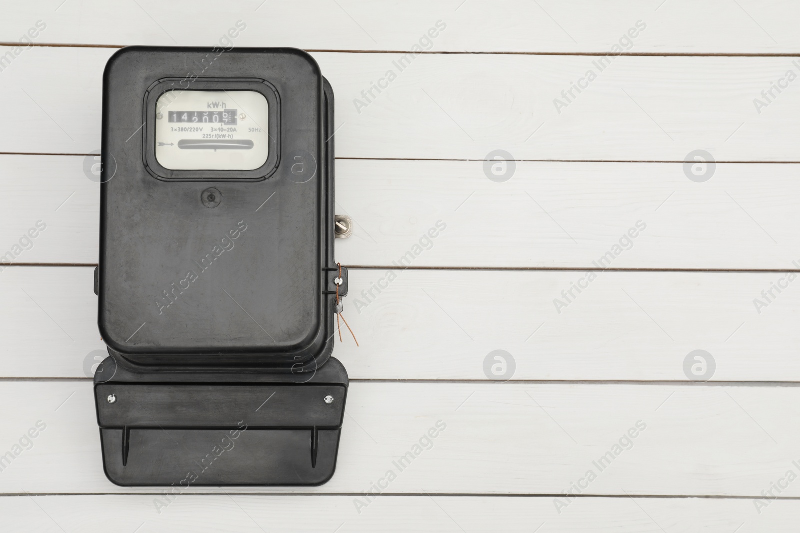Photo of Black electric meter on white wooden background, top view with space for text. Measuring device