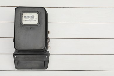 Photo of Black electric meter on white wooden background, top view with space for text. Measuring device