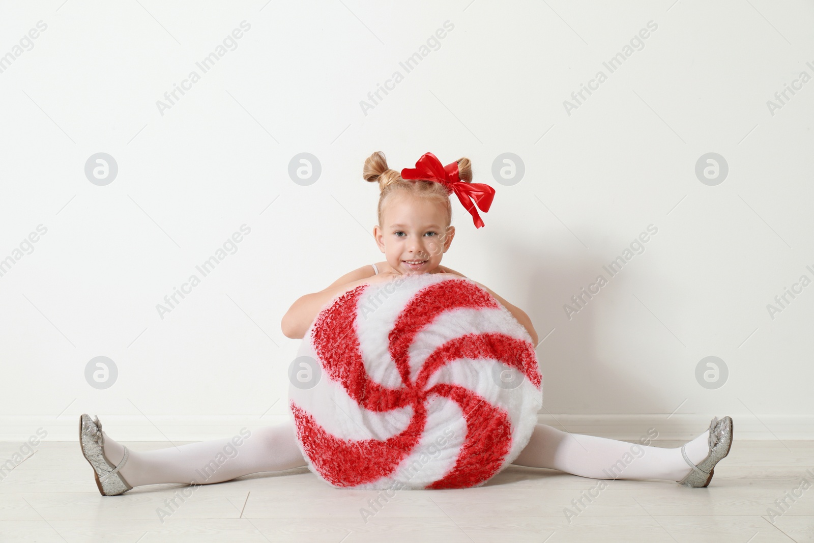 Image of Cute little girl dressed as candy sitting near white wall. Christmas suit