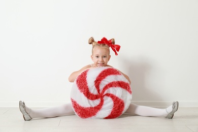 Cute little girl dressed as candy sitting near white wall. Christmas suit