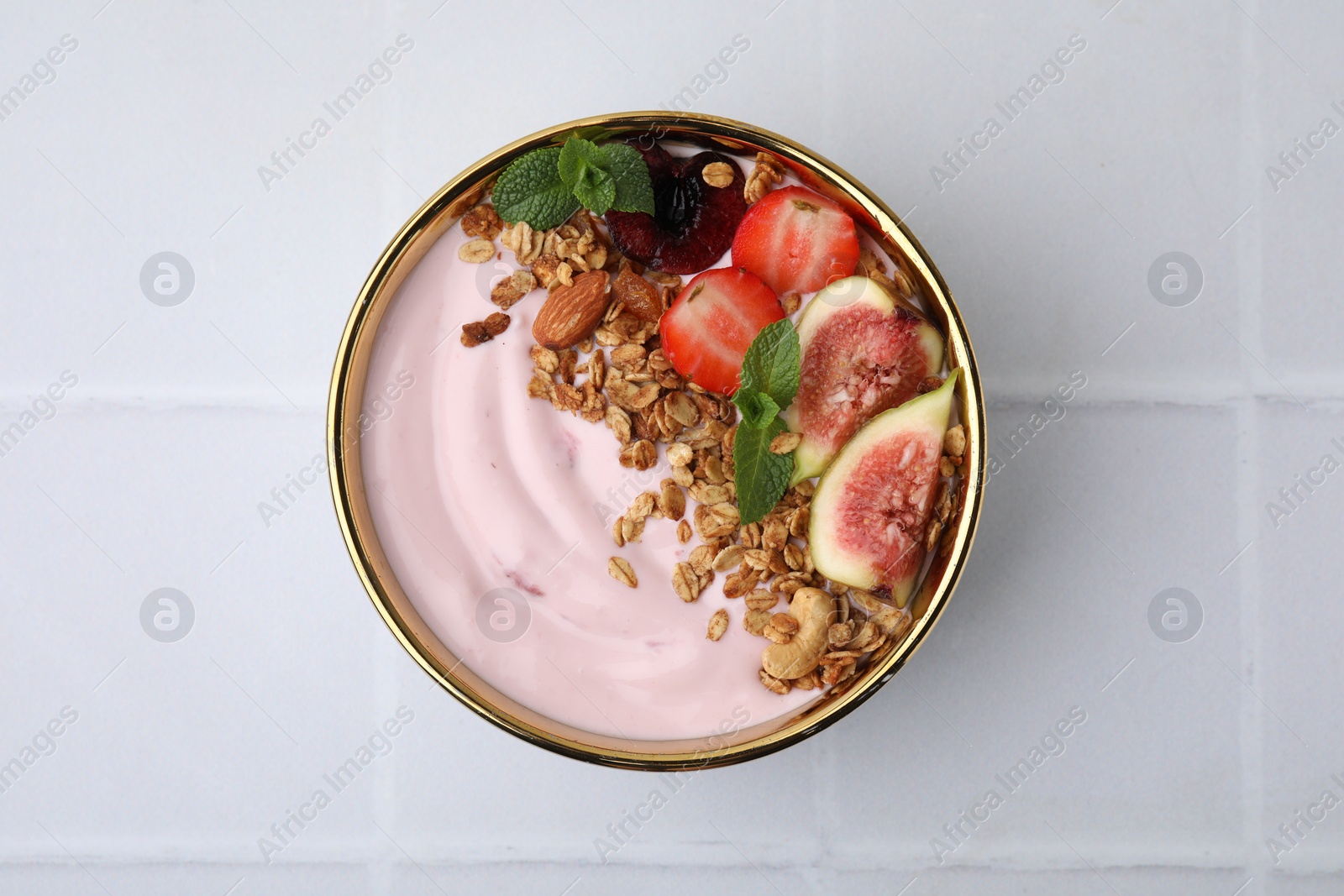 Photo of Bowl with yogurt, fruits and granola on white tiled table, top view