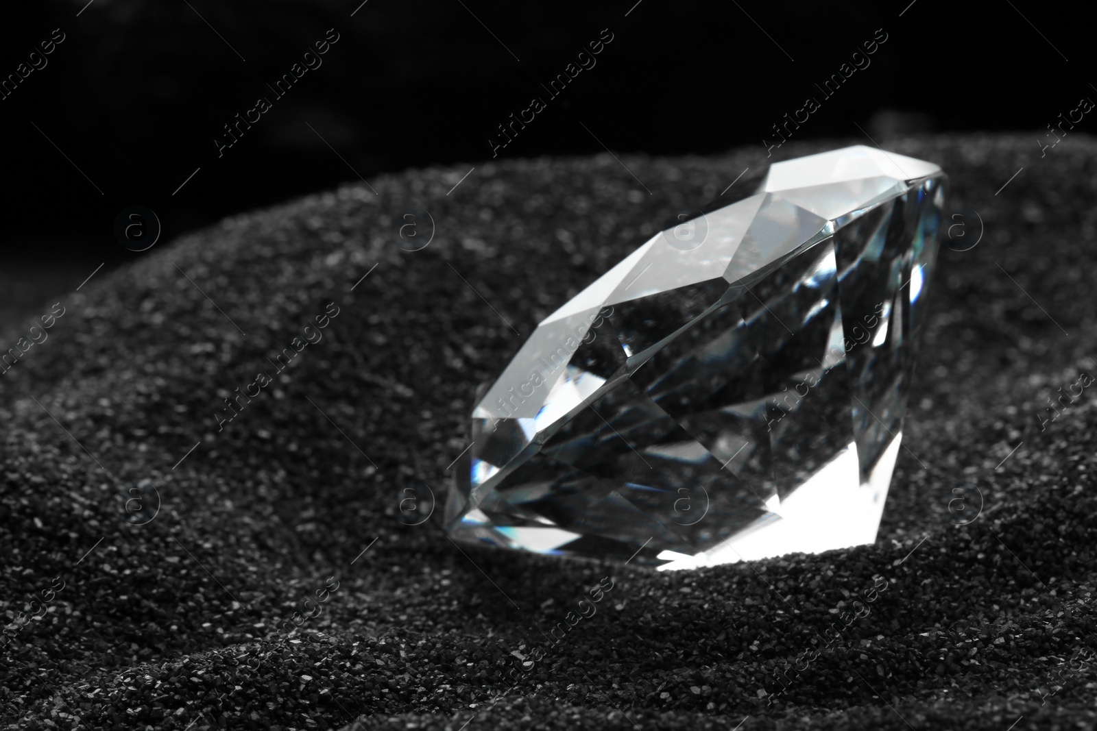 Photo of Beautiful shiny diamond on decorative black sand, closeup. Space for text