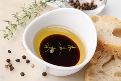 Photo of Bowl of organic balsamic vinegar with oil and spices served with bread slices on beige table, closeup