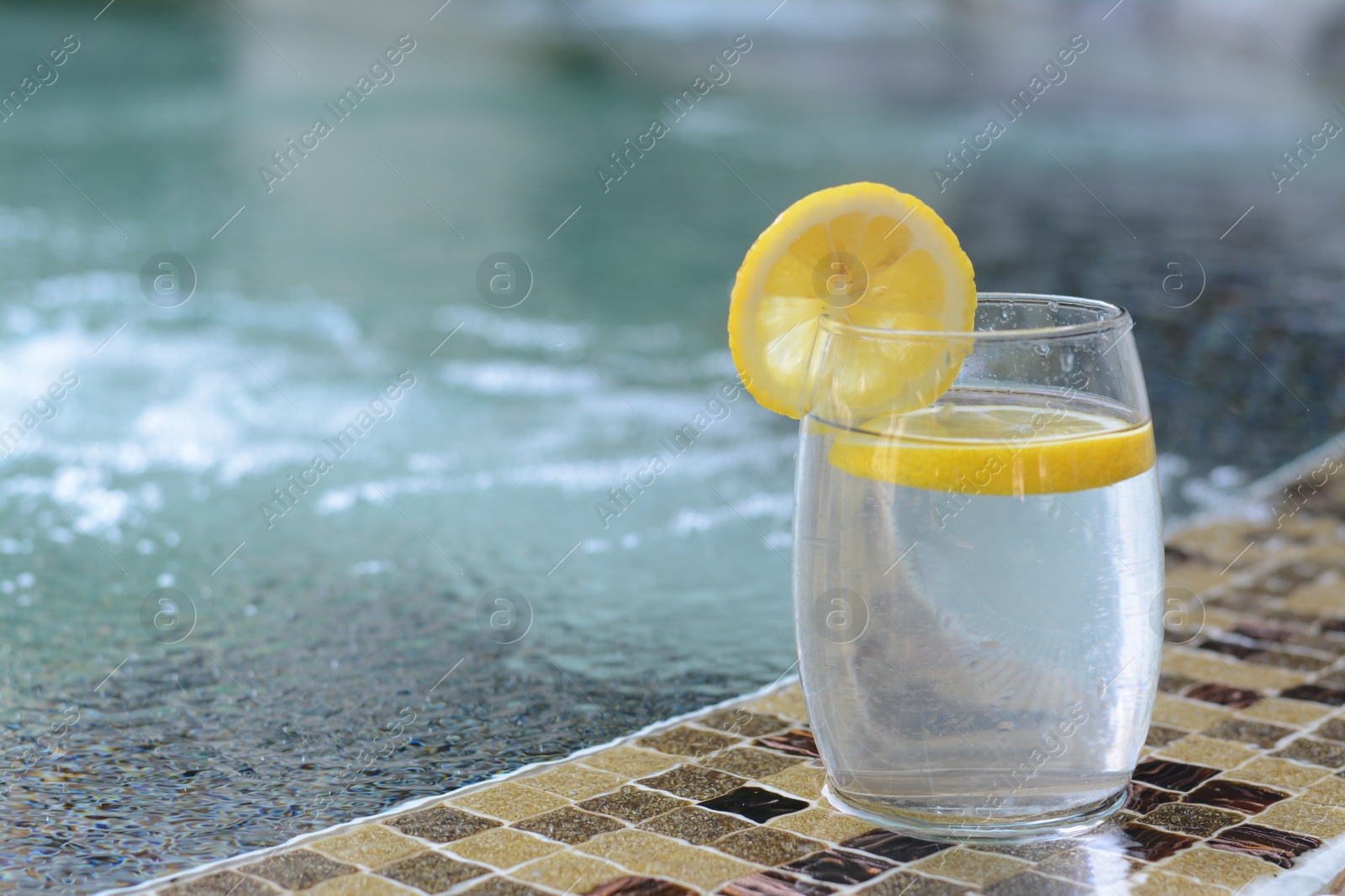 Photo of Refreshing water with lemon on edge of swimming pool, space for text