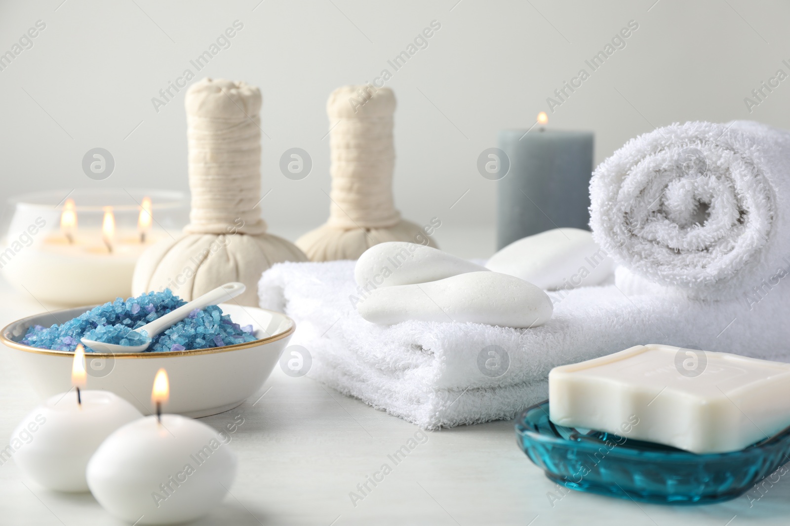 Photo of Spa composition. Towels, herbal bags, soap, sea salt and burning candles on light table