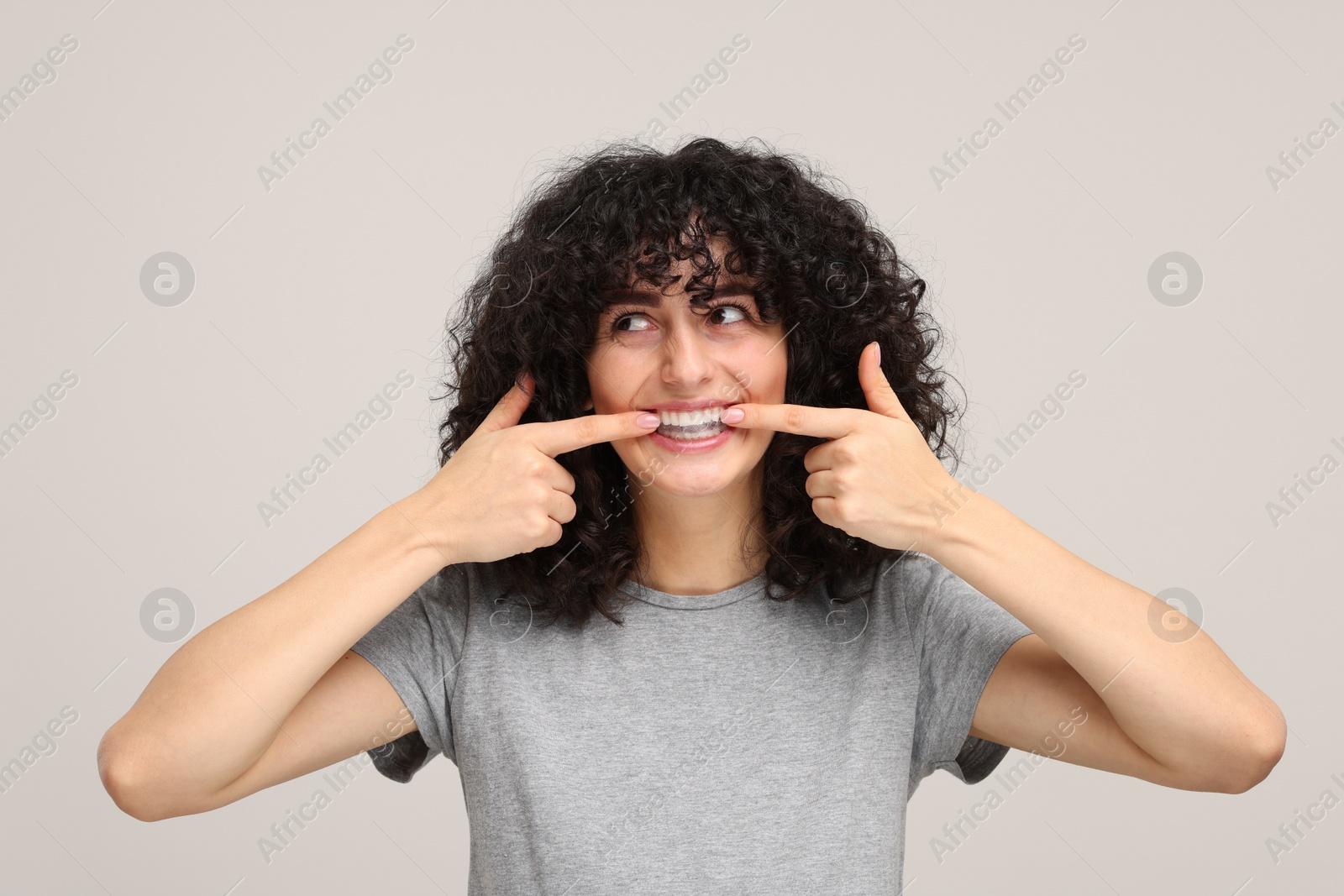 Photo of Young woman applying whitening strip on her teeth against light grey background