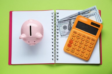 Photo of Piggy bank, notebook, calculator and banknotes on light green background, top view