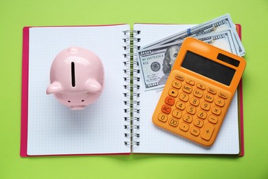 Piggy bank, notebook, calculator and banknotes on light green background, top view