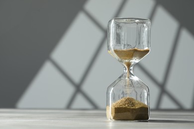 Photo of Hourglass with flowing gold sand on table against white wall, space for text