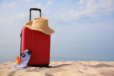Photo of Red suitcase with beach items on sandy seashore, space for text