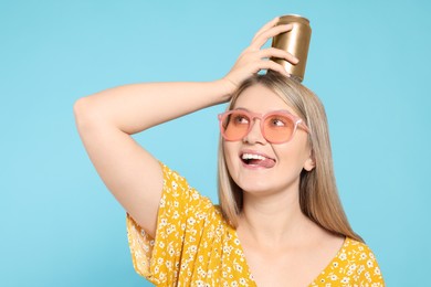 Beautiful happy woman holding beverage can against light blue background