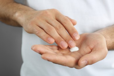 Photo of Man applying cream onto hand on grey background, closeup