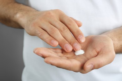 Man applying cream onto hand on grey background, closeup