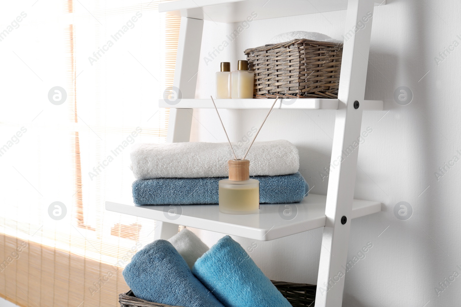 Photo of Shelving unit with clean towels and toiletries near white wall