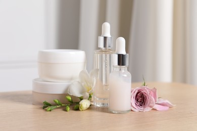 Bottles of cosmetic serum, cream jars and beautiful flowers on wooden table indoors