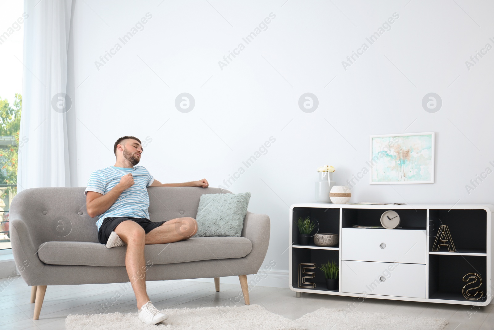 Photo of Young man suffering from heat at home. Air conditioner malfunction