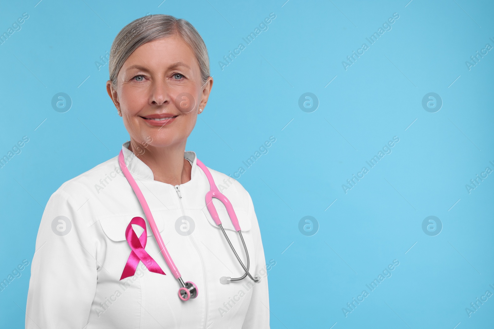 Photo of Doctor with pink ribbon and stethoscope on light blue background, space for text. Breast cancer awareness