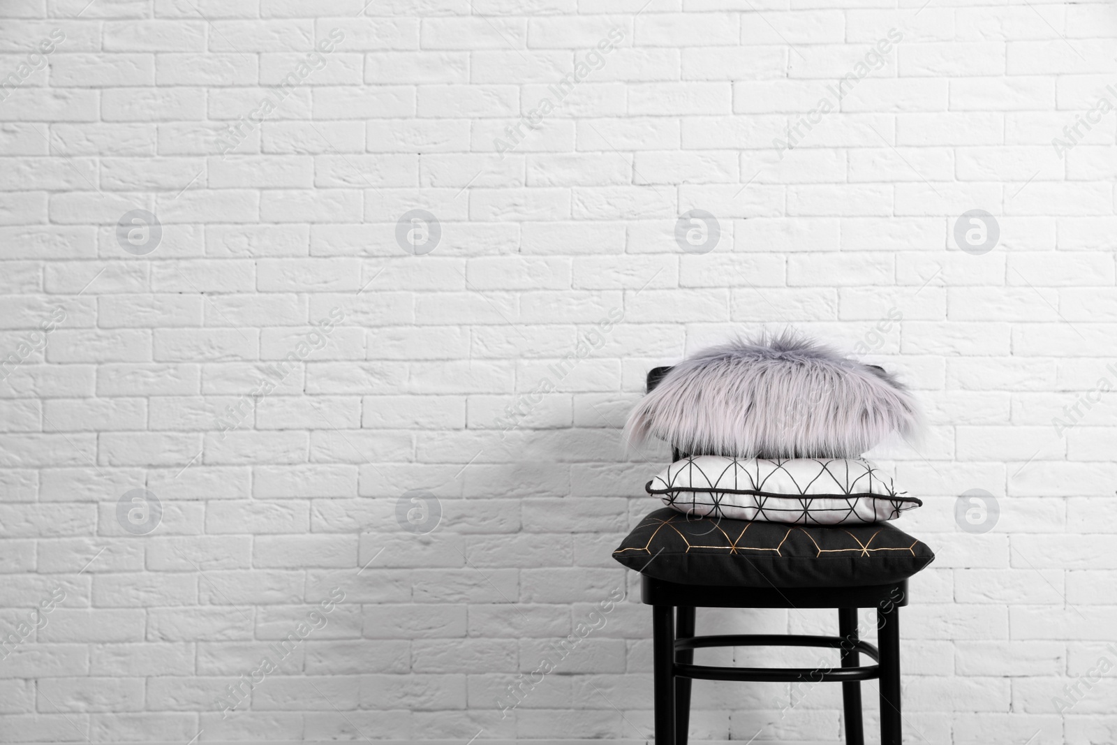 Photo of Many different pillows on chair near brick wall with space for text